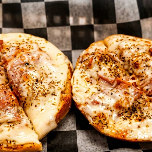 Two cheesy pizza bagels with pepperoni and herbs on black and white checkered paper.