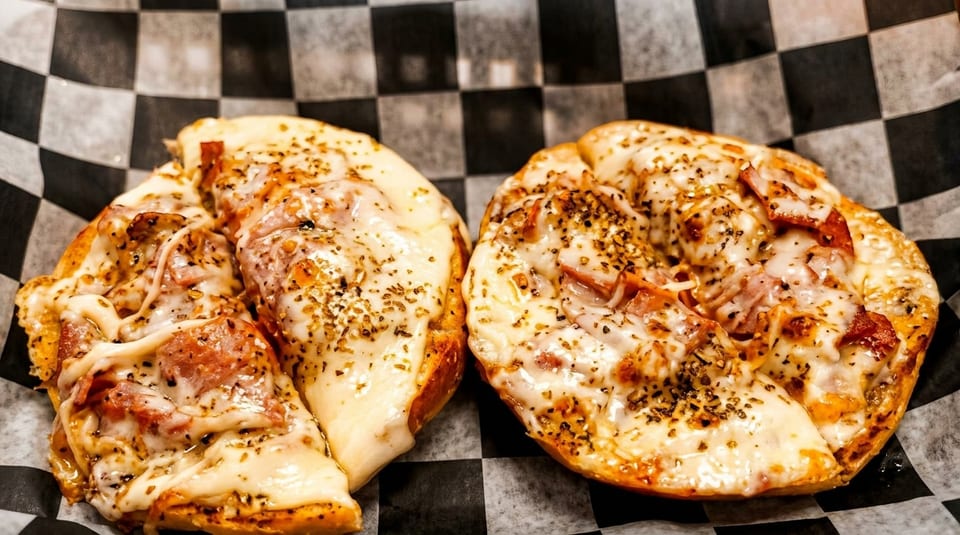 Two cheesy pizza bagels with pepperoni and herbs on black and white checkered paper.