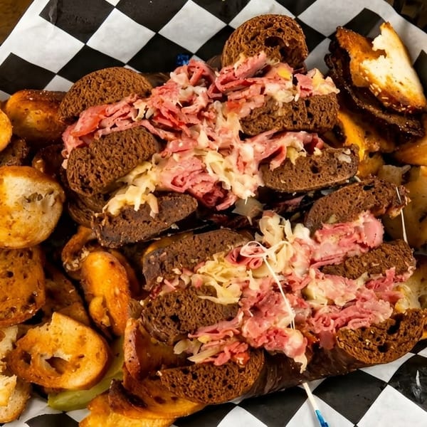 A basket of mini Reuben sandwiches on dark bread with sauerkraut, pastrami, and toasted bagel chips.