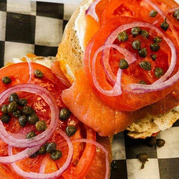 Lox bagel with cream cheese, tomatoes, red onions, and capers in a plastic container.