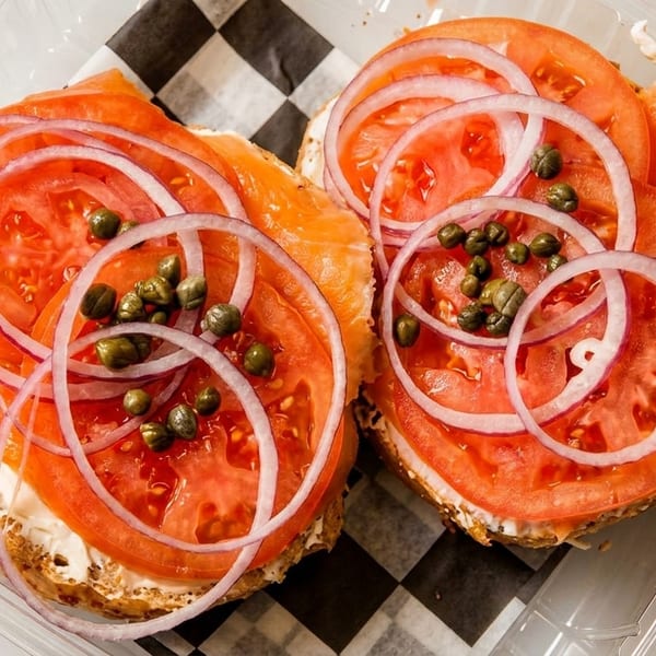 Two bagels with cream cheese, smoked salmon, tomato, red onion, and capers in a plastic container.